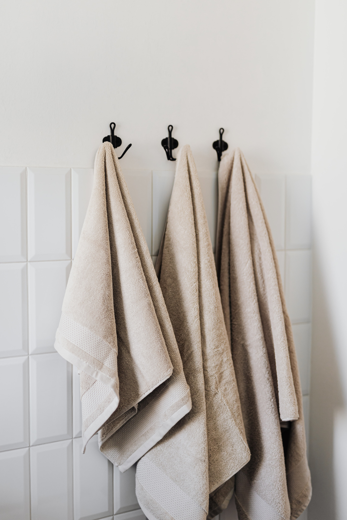 Set of beige towels on hooks in bathroom
